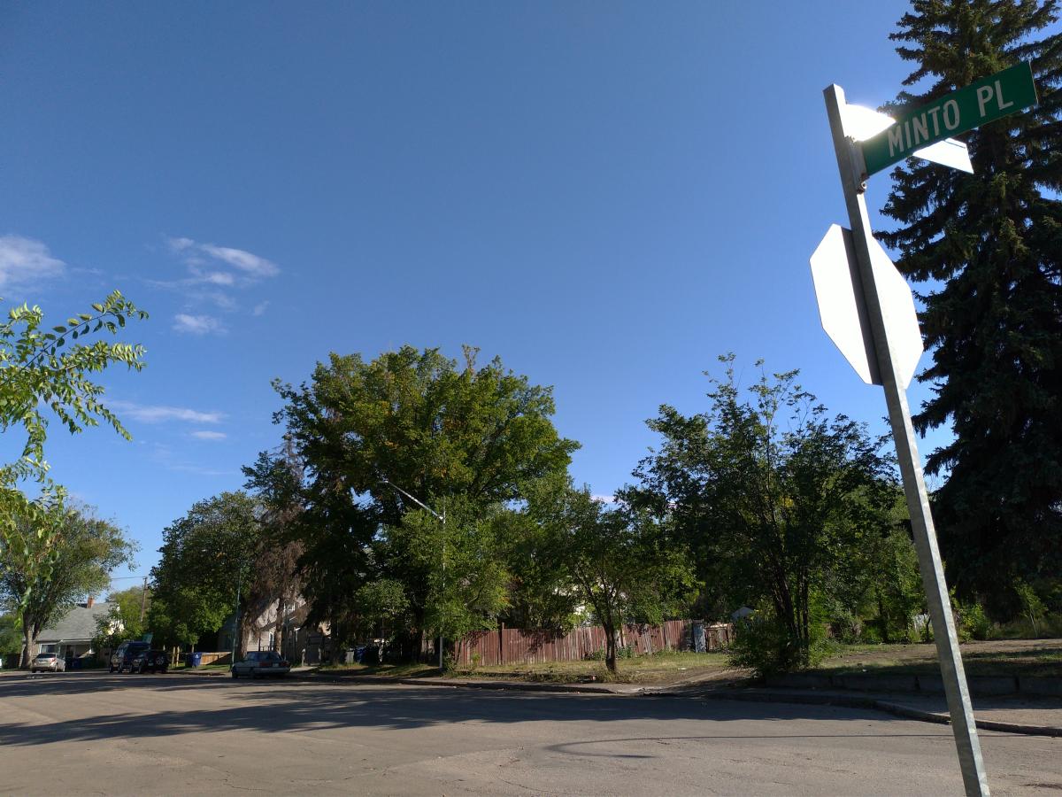 Street sign says Minto Place. Vacant lots in the foreground and houses in the background.